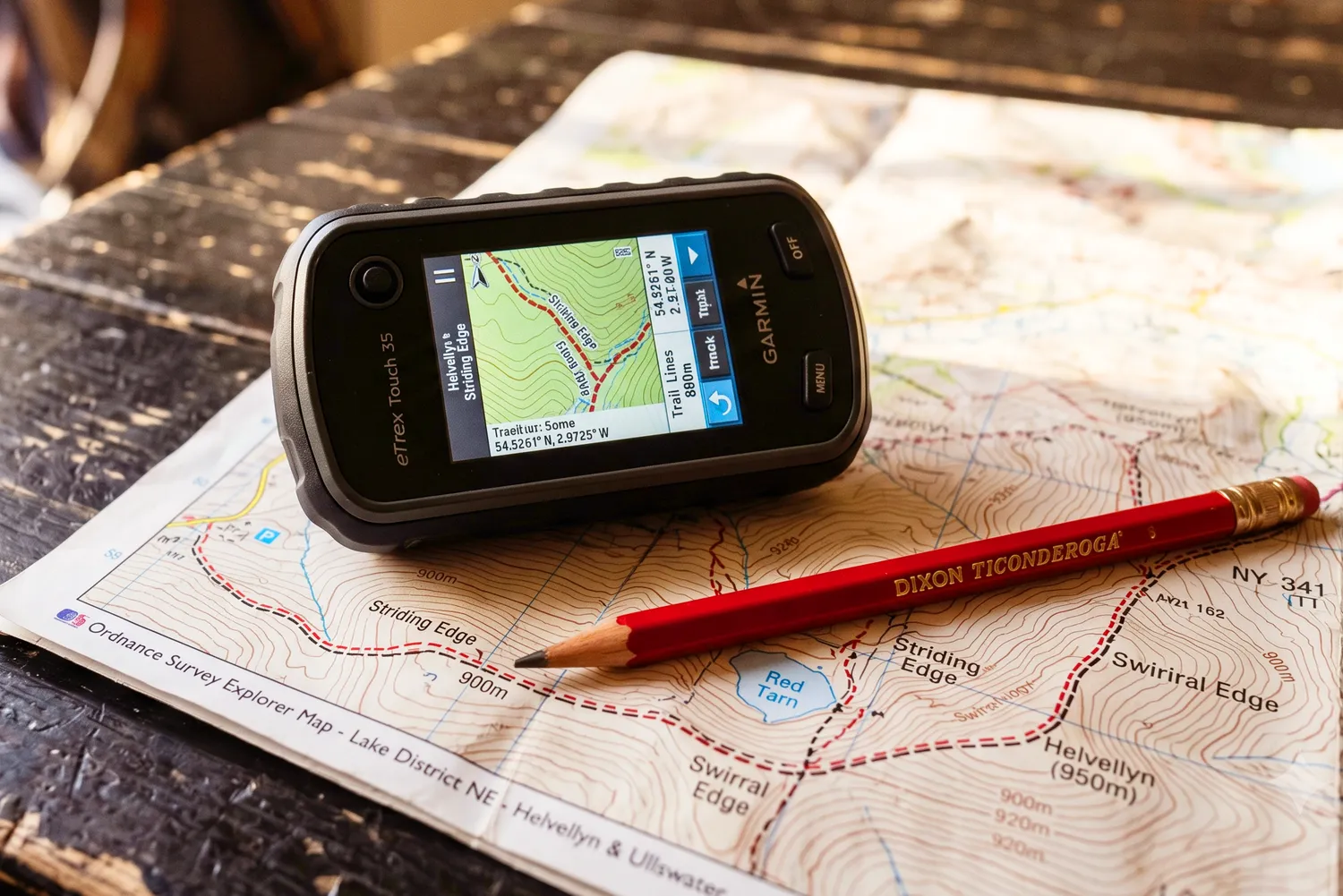 A handheld GPS navigator and a red pencil resting on a printed topographic map.