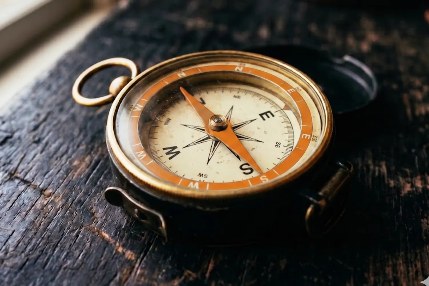 A brass compass with a copper bezel resting on weathered dark wood.